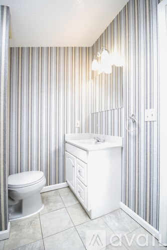 A bathroom with a toilet, sink and striped wallpaper.