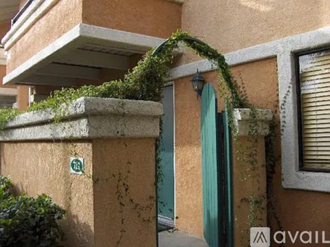A green door is on the right side of a building with a wall that is covered in vines.