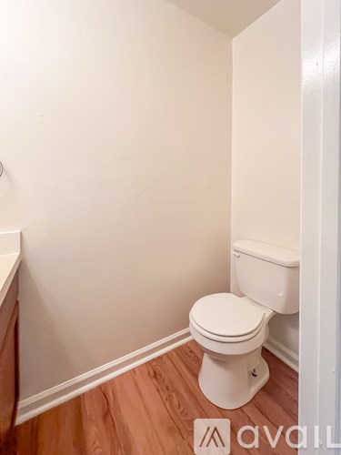 A white toilet in a small bathroom with wooden flooring.