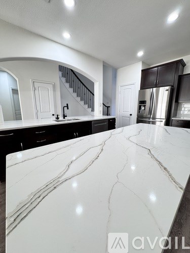A kitchen with a marble countertop and a staircase in the background.