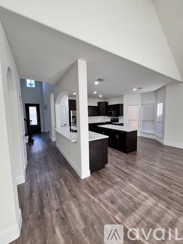 A spacious kitchen with dark wood flooring and white walls.