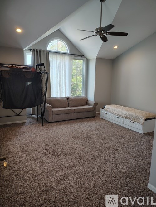 A room with a ceiling fan, a couch, a bed, and a window with curtains.