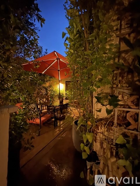 A patio with a table and chairs under a lit umbrella at night.