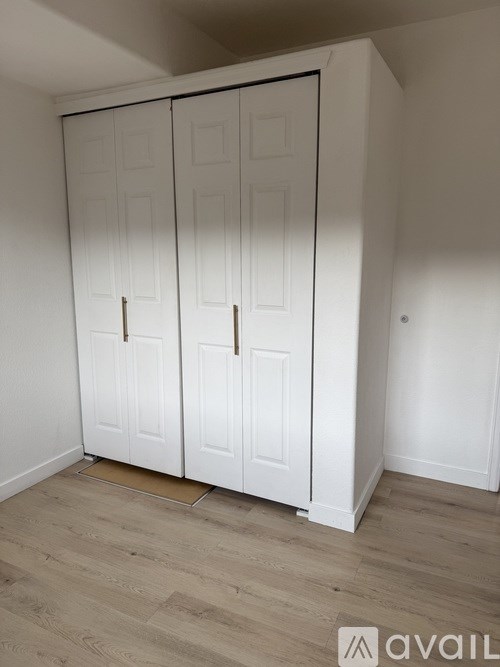 A white wardrobe with two doors is in a room with wooden flooring.