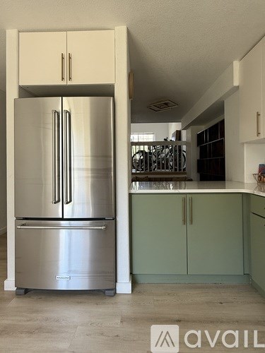 A stainless steel refrigerator in a kitchen with green cabinets.