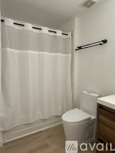 A white toilet sits next to a white shower curtain in a small bathroom.