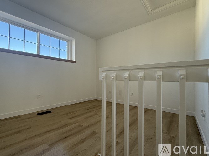 A room with wooden flooring and white walls, with a window on the left side.