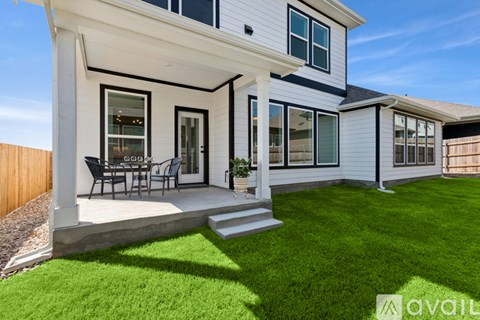 A house with a white exterior and a black roof has a patio with a table and chairs.