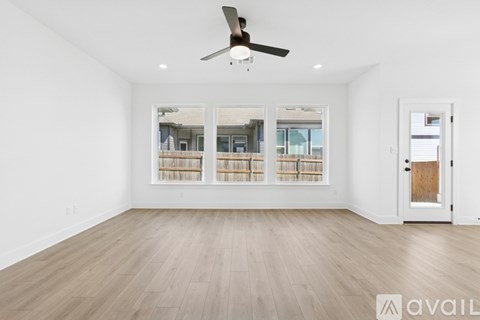 A room with a ceiling fan and a view of a balcony through the windows.