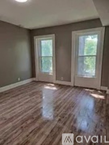 A room with wooden flooring and two windows.