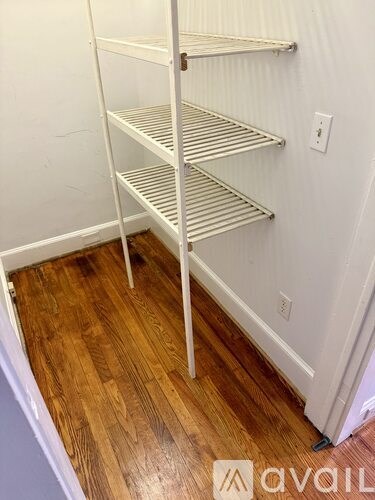 A white shelving unit with four shelves stands in a room with wooden flooring.