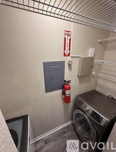A washing machine is in a small room with a fire extinguisher and a fire sign on the wall.