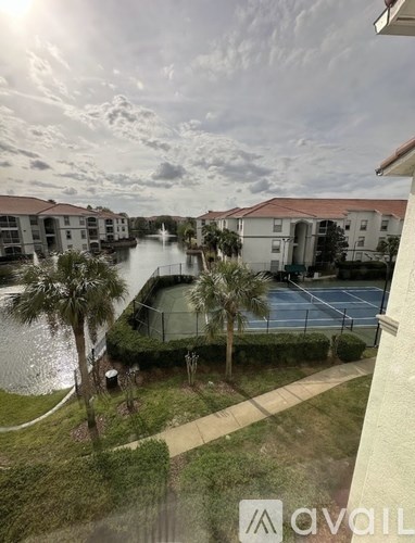 A view from a balcony overlooking a body of water with palm trees and a tennis court.