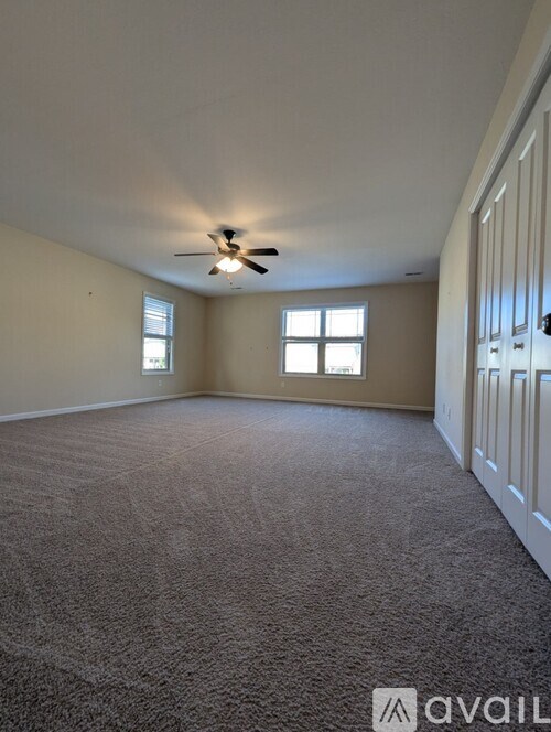A room with a carpeted floor, a ceiling fan, and two windows.