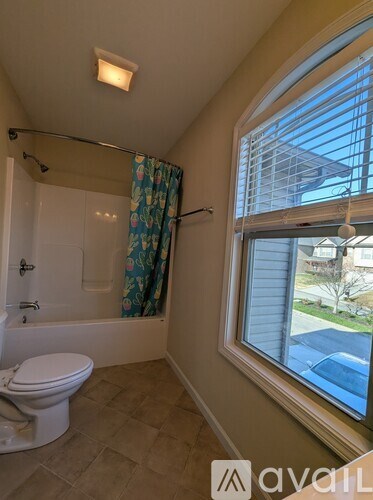 A bathroom with a toilet, a shower with a curtain, and a window.