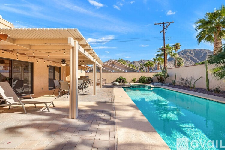 A pool in a backyard with a patio and chairs.