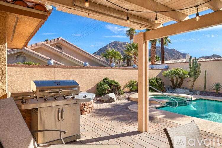A patio with a grill and a pool in a sunny backyard.
