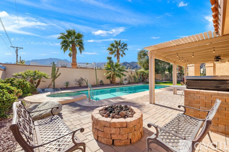 A patio with a fire pit and chairs overlooks a pool and palm trees.