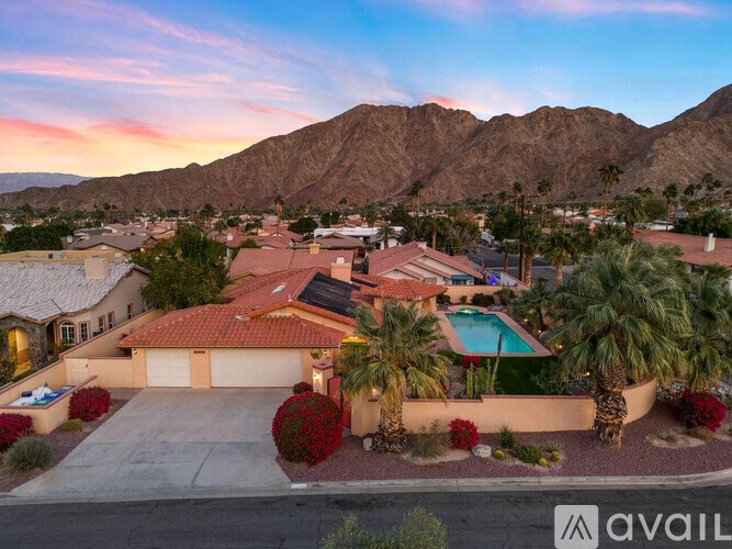 A house with a pool surrounded by palm trees and a mountain range in the background.