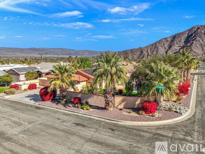A house surrounded by palm trees and red flowers with mountains in the background.