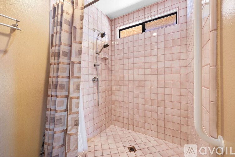 A shower with pink tiles and a white shower head.