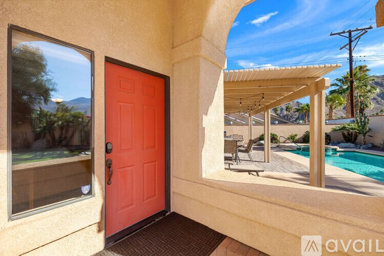 A red door is on the left side of a patio with a pool and a mountain in the background.