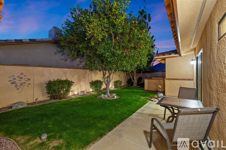 A backyard with a tree, lawn, and patio furniture.