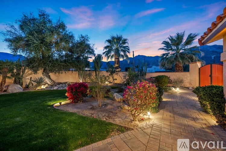 A beautifully landscaped garden with a pathway, trees, and bushes is illuminated by lights.