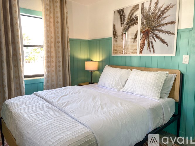 A bedroom with a large bed and a picture of palm trees on the wall.