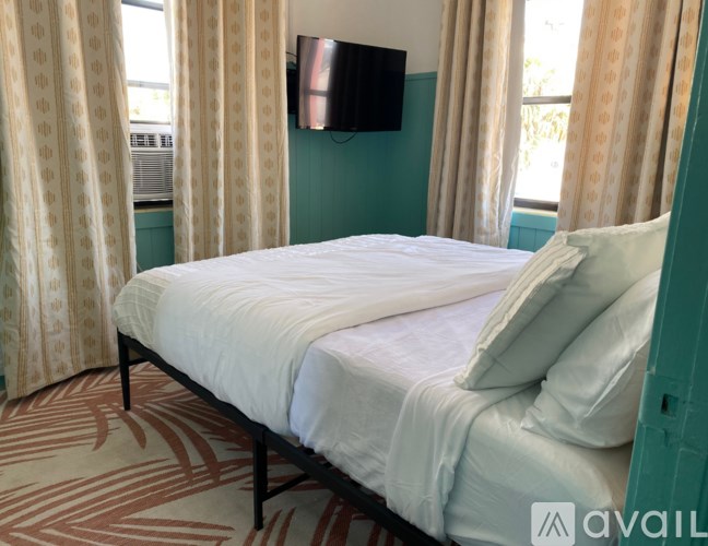 A bed with a white sheet and two pillows sits in a room with patterned carpeting.