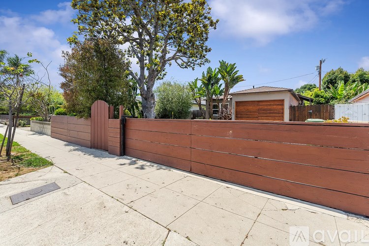 A brown fence with a tree and a house in the background.