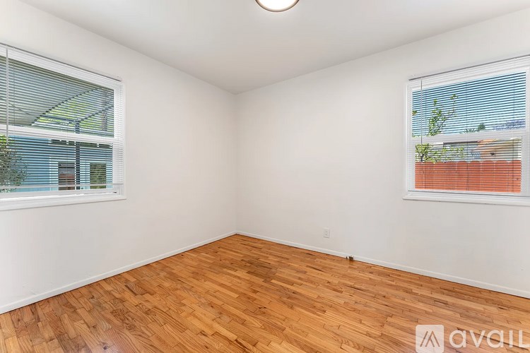 A room with wooden flooring and two windows with blinds.