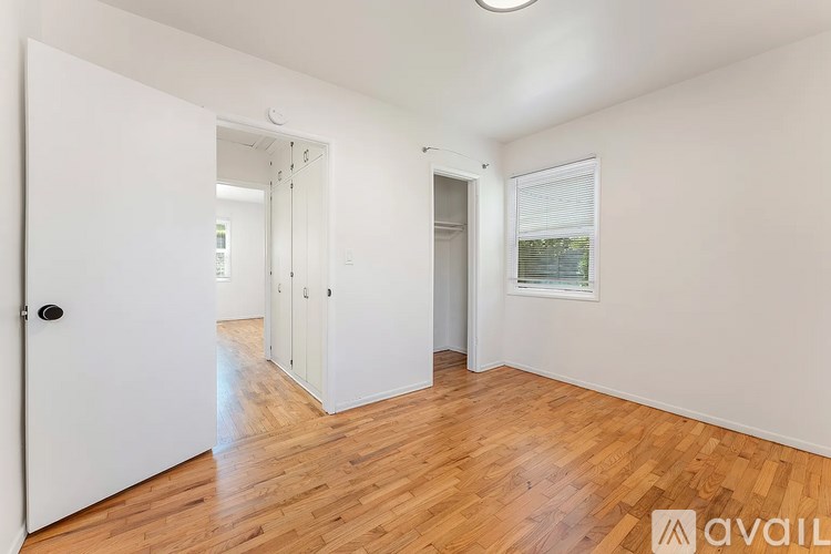A room with wooden floors and white walls, with a door on the left and a window on the right.