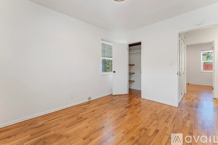 A room with wooden floors and white walls, with a window and a door visible.
