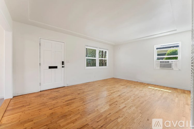 A room with wooden flooring and white walls, featuring a door, a window, and a picture on the wall.