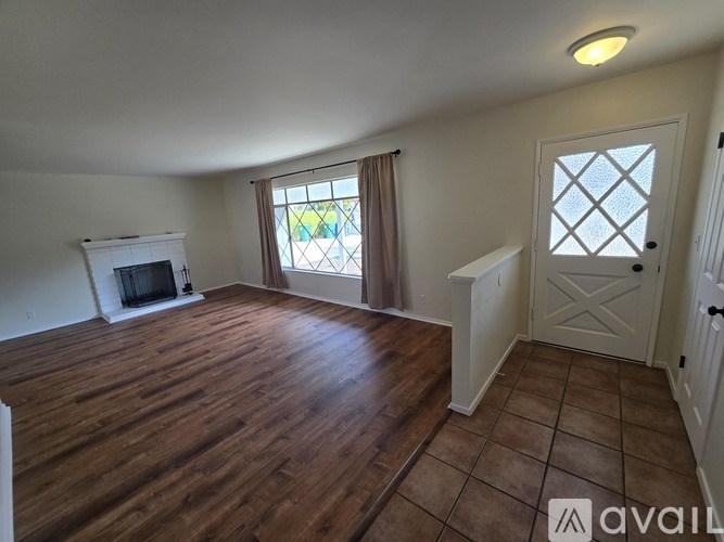 A room with wooden flooring and a window with a view of a backyard.