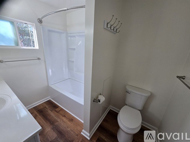 A white toilet in a small bathroom with wood flooring and a shower.