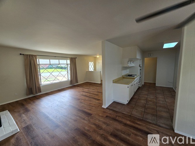 A room with wooden flooring and a window with a view of a green field.