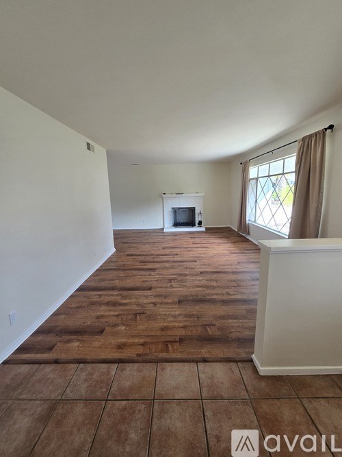 A room with wooden flooring and a window with curtains.