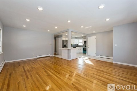A spacious room with wooden flooring and a kitchen area in the background.