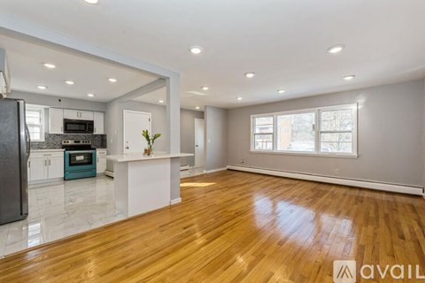 A spacious kitchen with wooden floors and a refrigerator on the left side.