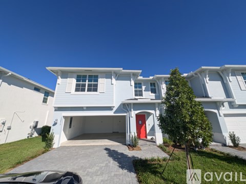 A white two-story house with a red door and a tree in front.