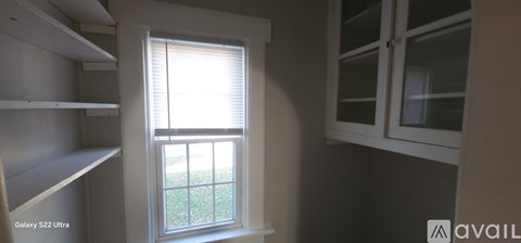 A window with blinds in a room with white shelves.