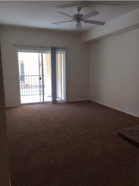 an empty living room with a ceiling fan and a door to a balcony