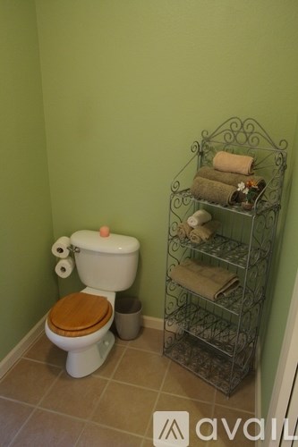 A toilet with a wooden seat and a towel rack with towels on it.