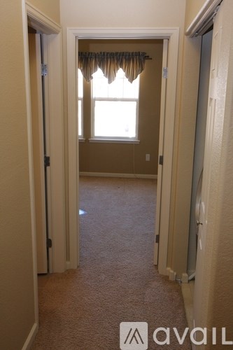 A hallway with a carpeted floor and a window with curtains.