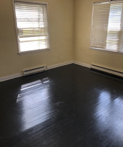 A room with a black floor and two windows with blinds.