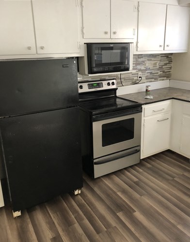 A black fridge and stove in a kitchen with white cabinets.
