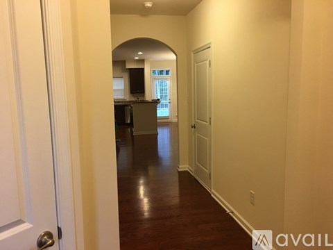 A hallway with a door on the left and a kitchen in the distance.