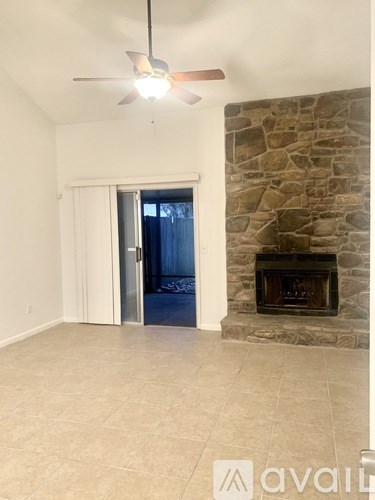 A room with a stone fireplace and a ceiling fan.
